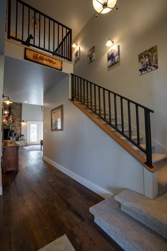 staircase with a stone fireplace, a towering ceiling, and wood-type flooring