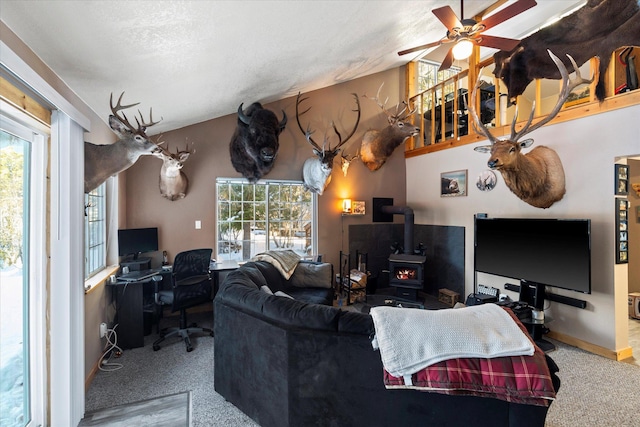 living room featuring carpet floors, a wood stove, ceiling fan, and a healthy amount of sunlight