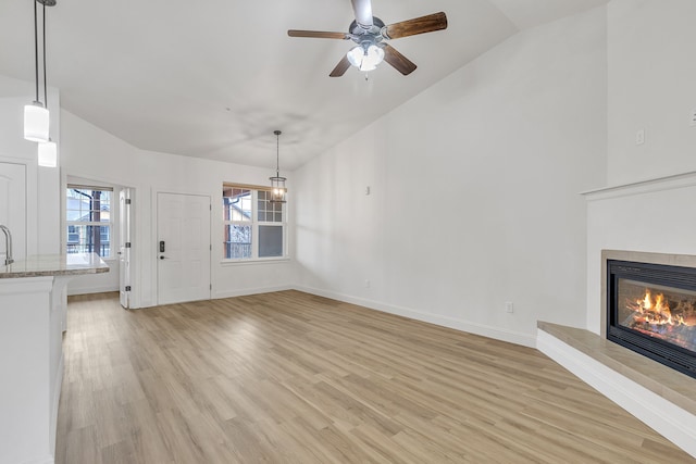 unfurnished living room featuring lofted ceiling, ceiling fan, light wood-type flooring, and a tile fireplace