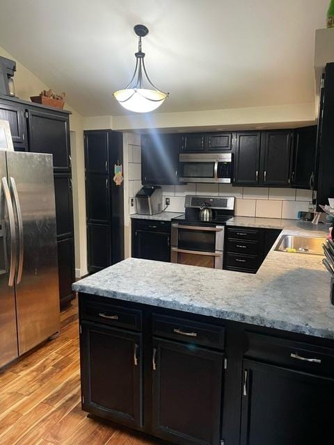 kitchen with vaulted ceiling, sink, hanging light fixtures, light hardwood / wood-style floors, and stainless steel appliances