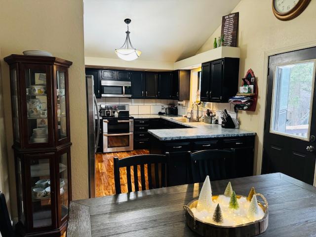 kitchen featuring lofted ceiling, sink, pendant lighting, stainless steel appliances, and backsplash