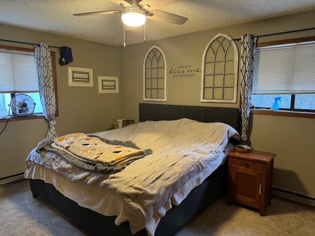 carpeted bedroom featuring multiple windows, ceiling fan, a textured ceiling, and baseboard heating