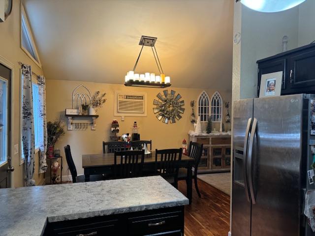 kitchen featuring dark wood-type flooring, lofted ceiling, decorative light fixtures, and stainless steel fridge with ice dispenser