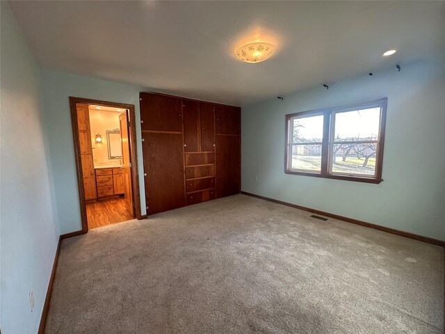 unfurnished bedroom featuring ensuite bathroom, light colored carpet, and a closet