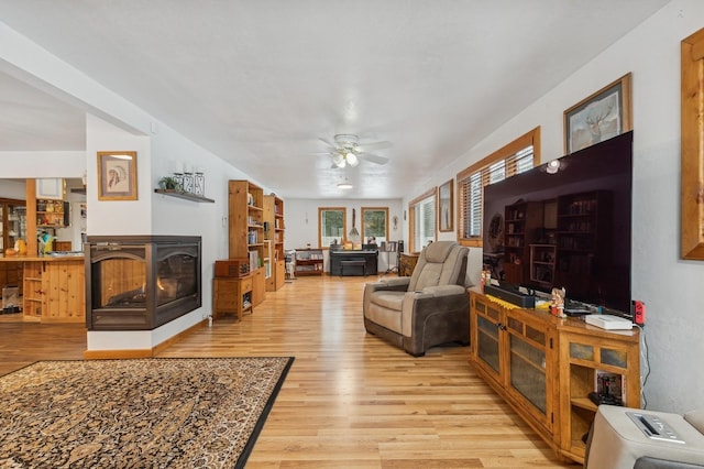 living area with ceiling fan, a multi sided fireplace, and wood finished floors