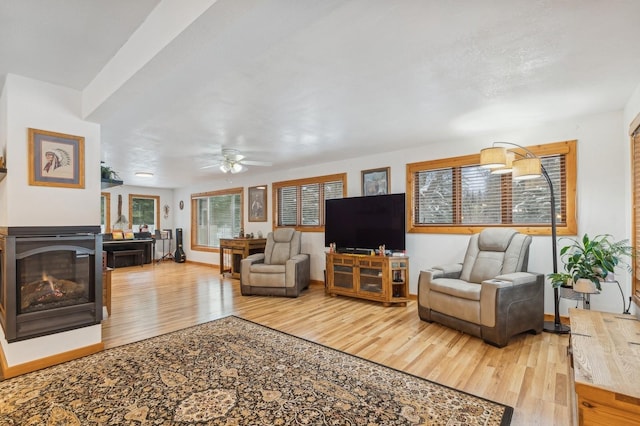 living room with a glass covered fireplace, ceiling fan, baseboards, and wood finished floors