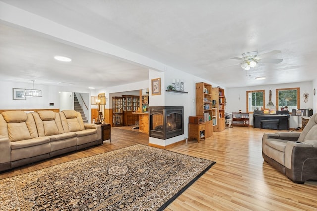 living room with a multi sided fireplace, ceiling fan, and light wood-type flooring