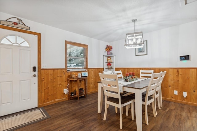 dining room with a chandelier, wooden walls, and dark wood-type flooring