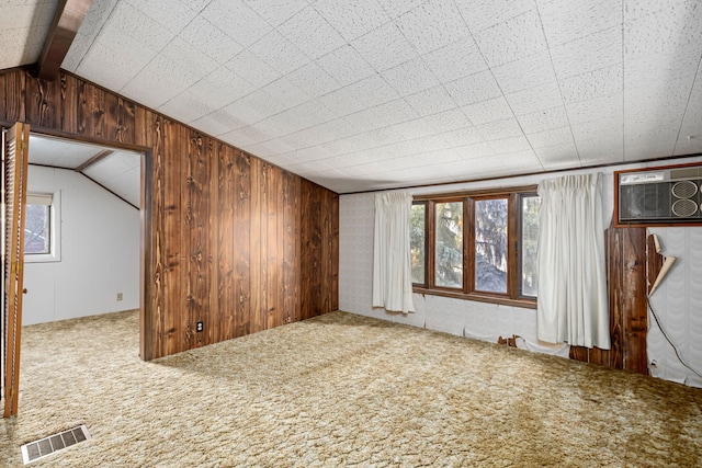 carpeted empty room featuring a wall unit AC, wooden walls, and lofted ceiling with beams