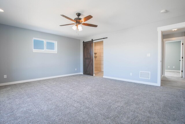 carpeted spare room featuring ceiling fan and a barn door