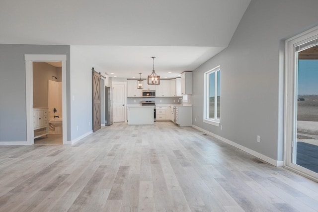 unfurnished living room featuring a barn door, light hardwood / wood-style flooring, a chandelier, and sink