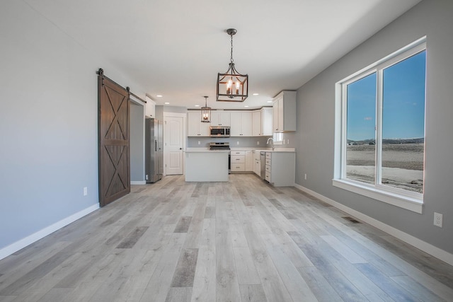 kitchen featuring stainless steel appliances, white cabinets, hanging light fixtures, a barn door, and a notable chandelier