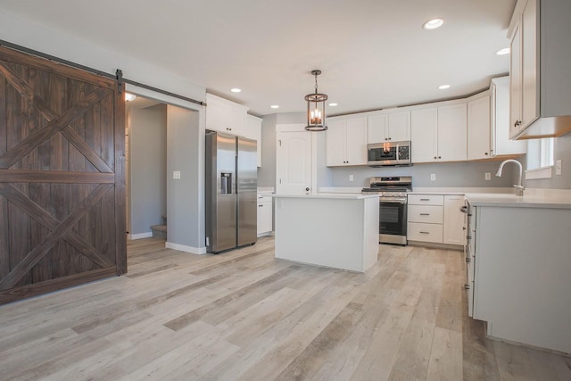 kitchen featuring a barn door, stainless steel appliances, hanging light fixtures, a center island, and white cabinets