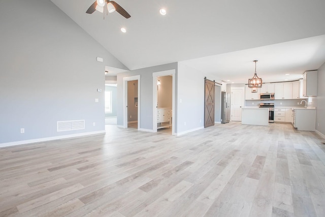 unfurnished living room featuring high vaulted ceiling, light wood-type flooring, a barn door, ceiling fan, and sink