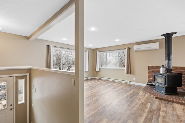 living room with an AC wall unit, a wood stove, a wealth of natural light, and a baseboard radiator