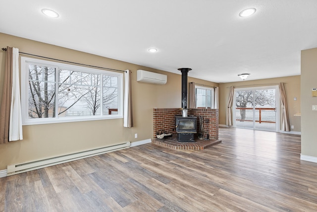 unfurnished living room with a baseboard radiator, a wood stove, hardwood / wood-style flooring, and a wall unit AC