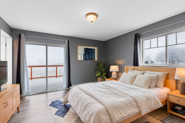 bedroom featuring a water view, light wood-type flooring, and multiple windows