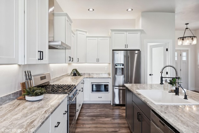 kitchen featuring white cabinetry, sink, wall chimney exhaust hood, hanging light fixtures, and stainless steel appliances