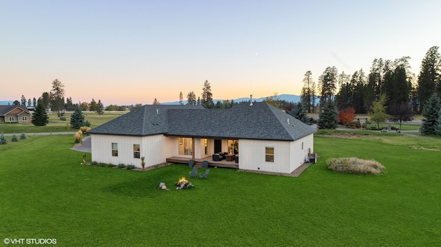 back house at dusk featuring a lawn