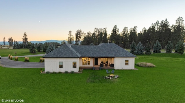 back house at dusk featuring a lawn