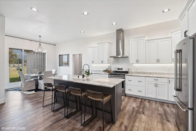 505 Sweetgrass Ranch Rd, Kalispell, MT 59901 - kitchen featuring stainless steel appliances, wall chimney exhaust hood, light stone counters, white cabinetry, and a kitchen bar