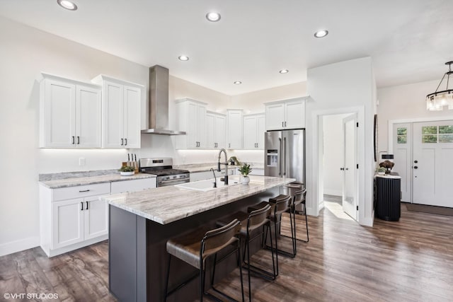 kitchen featuring stainless steel appliances, sink, wall chimney range hood, white cabinets, and an island with sink