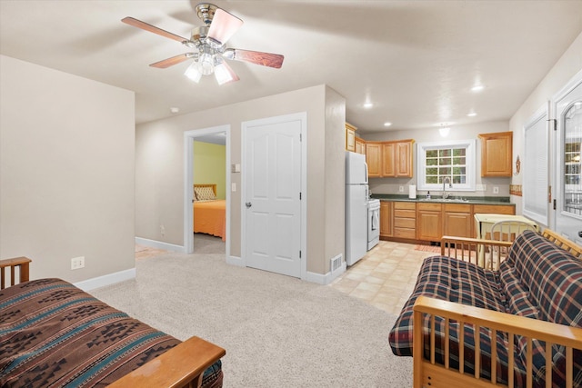 kitchen with light brown cabinetry, freestanding refrigerator, light carpet, a sink, and baseboards