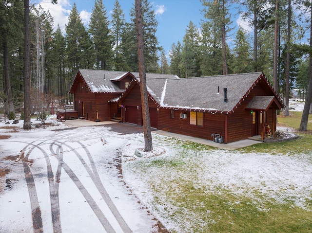 snow covered house featuring a garage and roof with shingles