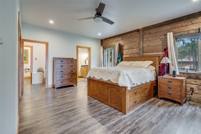 bedroom with ceiling fan, wood-type flooring, ensuite bathroom, and wooden walls