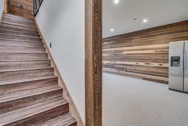 stairs with carpet and wood walls