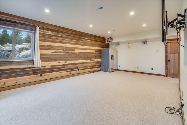 interior space with carpet flooring, stainless steel fridge, and wood walls