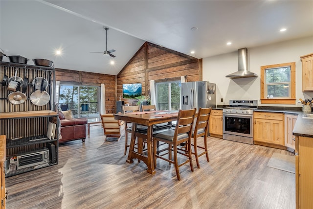 kitchen with wall chimney exhaust hood, wood walls, plenty of natural light, and appliances with stainless steel finishes