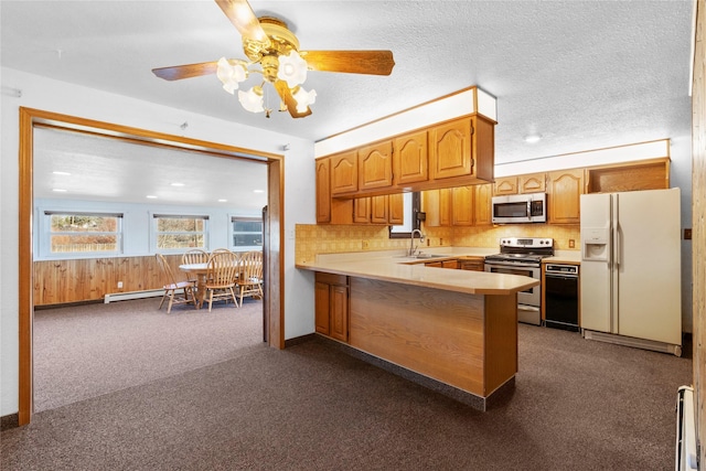 kitchen featuring a peninsula, a sink, light countertops, appliances with stainless steel finishes, and dark carpet