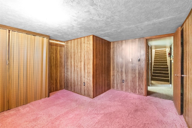 spare room featuring a textured ceiling, stairway, wood walls, and carpet