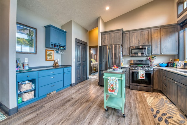 kitchen with appliances with stainless steel finishes, a textured ceiling, light hardwood / wood-style flooring, and dark stone countertops