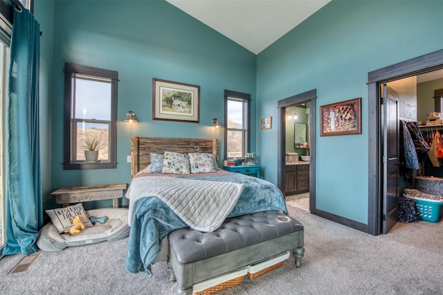 carpeted bedroom featuring a closet, a walk in closet, high vaulted ceiling, and ensuite bath