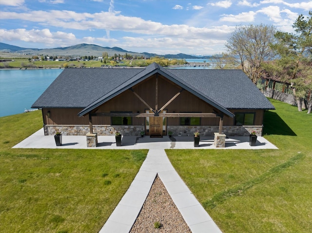 exterior space with stone siding, a patio area, a front lawn, and a water and mountain view