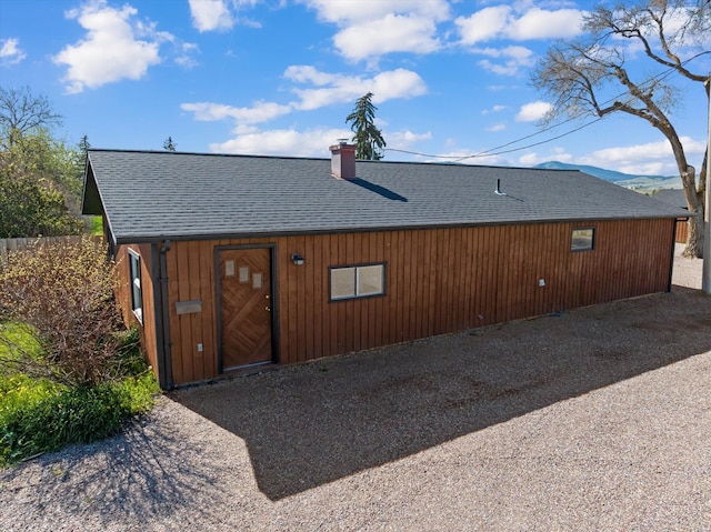 back of house featuring roof with shingles and a chimney