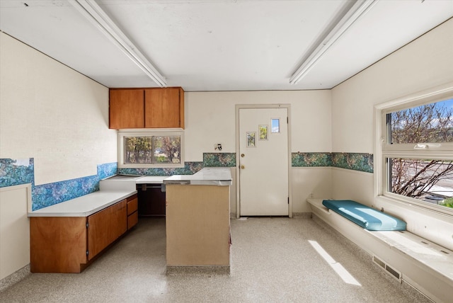 kitchen featuring black dishwasher, visible vents, brown cabinetry, a center island, and light countertops