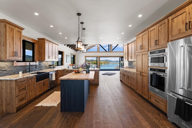 kitchen with stainless steel appliances, a kitchen island, a sink, hanging light fixtures, and wooden counters