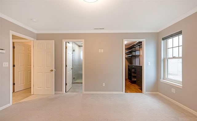 unfurnished bedroom featuring a walk in closet, ensuite bath, light colored carpet, crown molding, and a closet