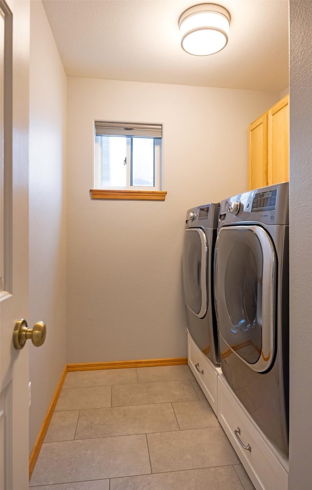 clothes washing area featuring cabinets, light tile patterned floors, and washer and clothes dryer