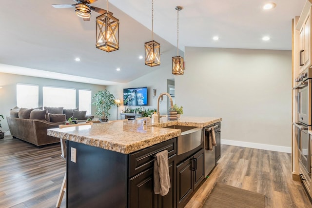 kitchen with ceiling fan, sink, a kitchen breakfast bar, dark hardwood / wood-style flooring, and a center island with sink