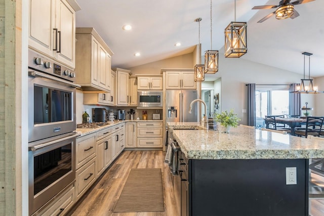 kitchen with vaulted ceiling, a large island with sink, decorative light fixtures, and appliances with stainless steel finishes