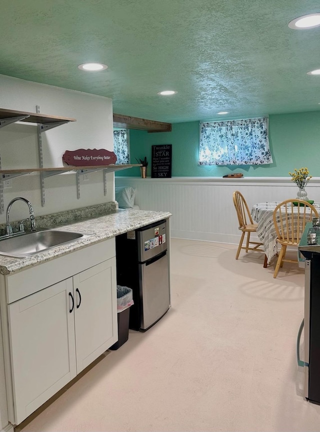 kitchen with stainless steel fridge, light colored carpet, white cabinetry, and sink