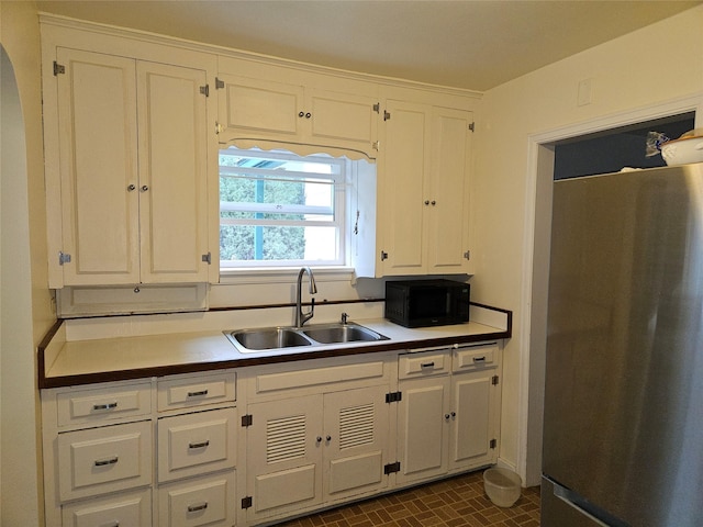 kitchen featuring stainless steel fridge, white cabinetry, and sink