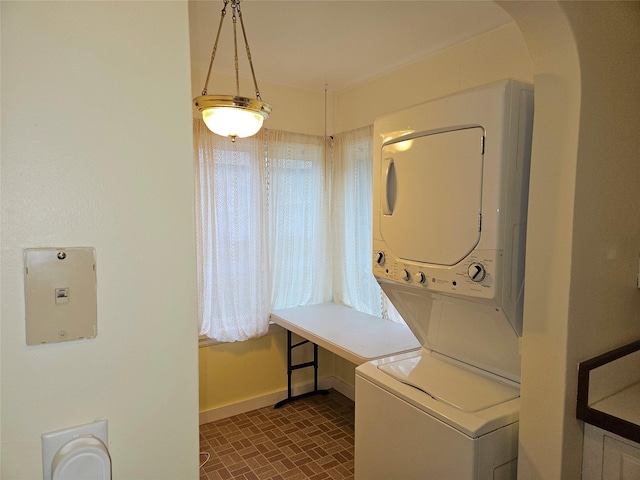 laundry room featuring stacked washer / drying machine and dark tile patterned floors