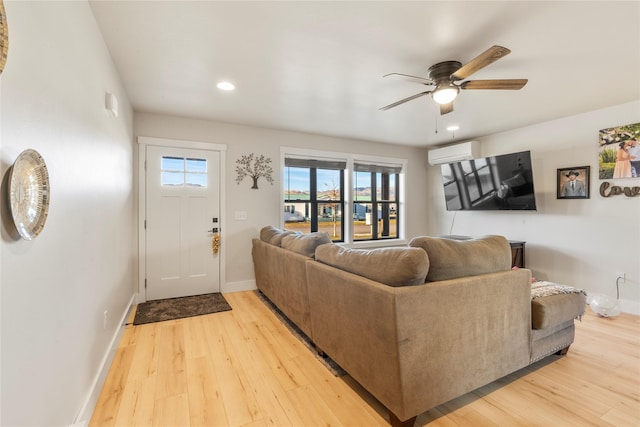 living room featuring ceiling fan, a healthy amount of sunlight, a wall unit AC, and light hardwood / wood-style flooring