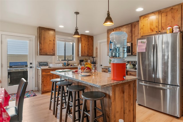 kitchen with a center island, hanging light fixtures, light hardwood / wood-style flooring, appliances with stainless steel finishes, and light stone counters