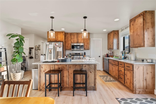 kitchen featuring sink, stainless steel appliances, light hardwood / wood-style flooring, pendant lighting, and a kitchen island